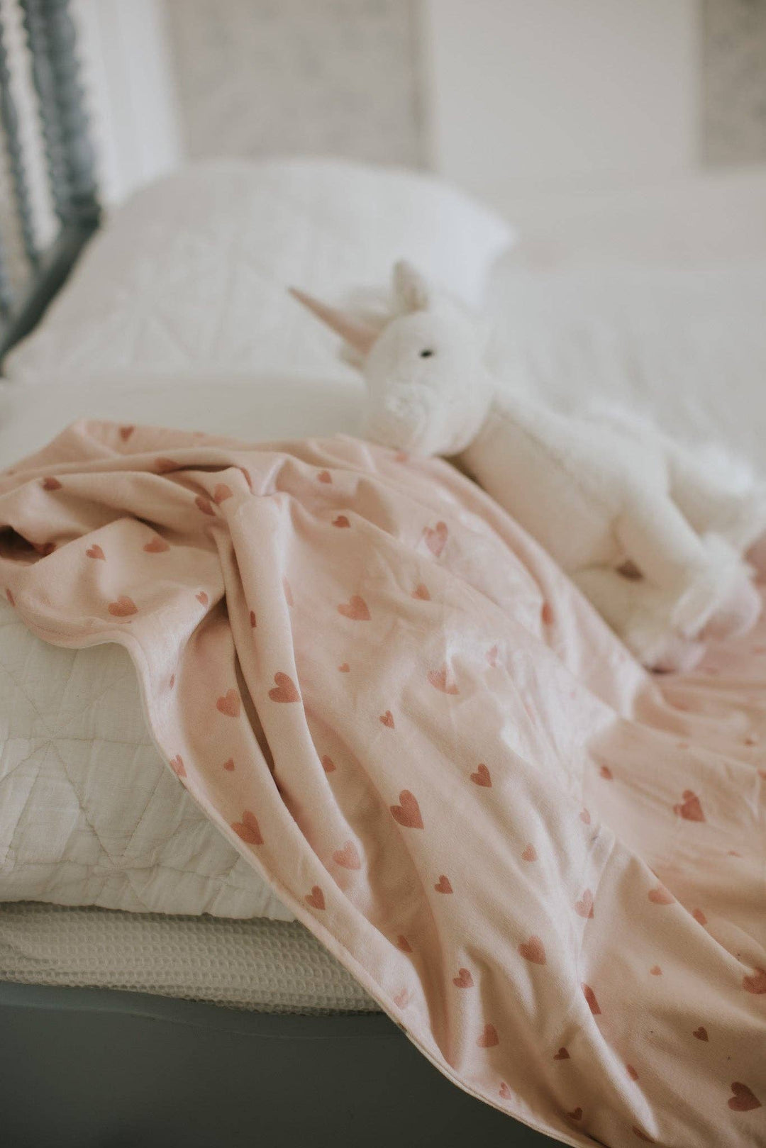 White unicorn toy on a pink blanket with heart patterns on a white surface