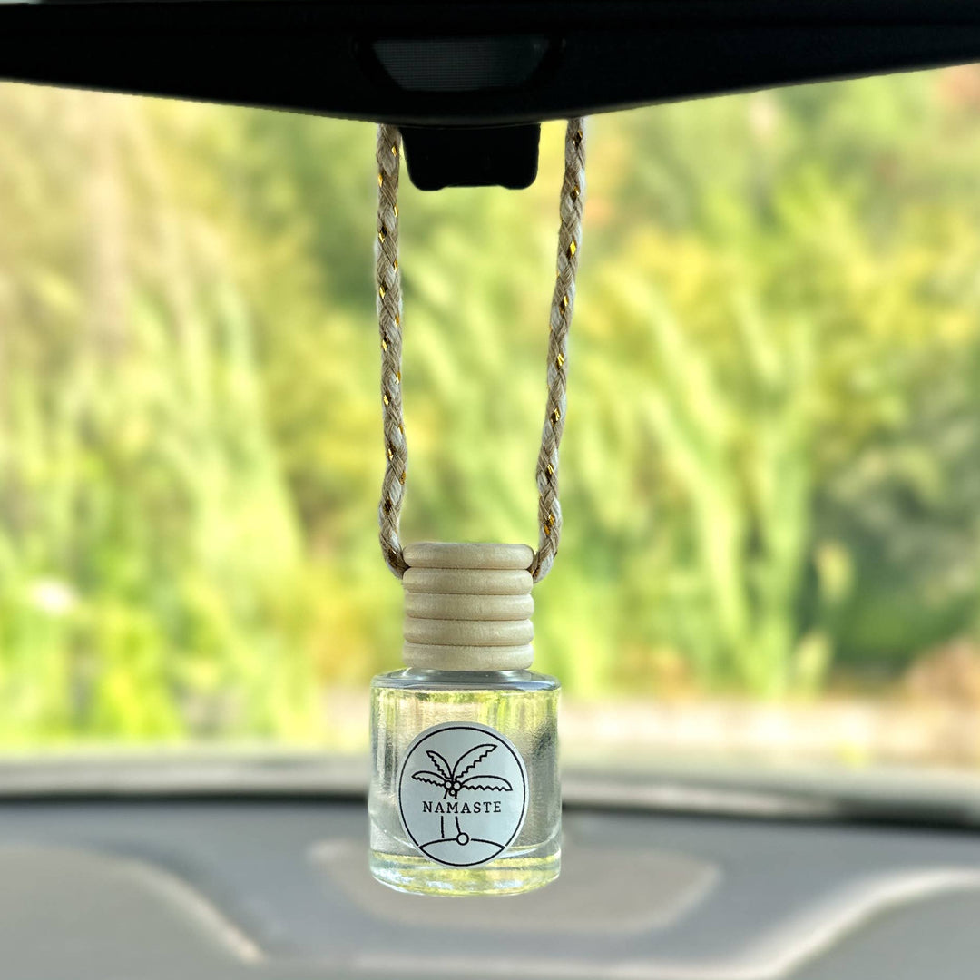 Car air freshener hanging from a rearview mirror with a blurred green outdoor background
