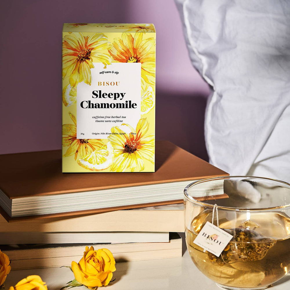 Sleepy Chamomile tea packaging with a glass of tea and yellow flowers on a light surface.
