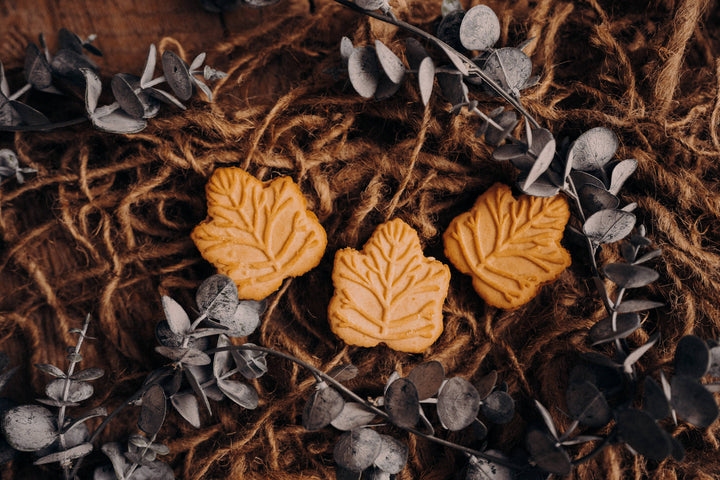 Three leaf-shaped cookies on a textured surface with eucalyptus leaves