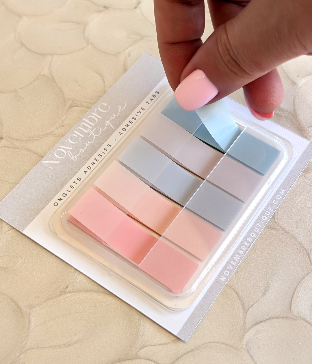 Set of adhesive tabs in pastel colors on a branded card, held by a hand.