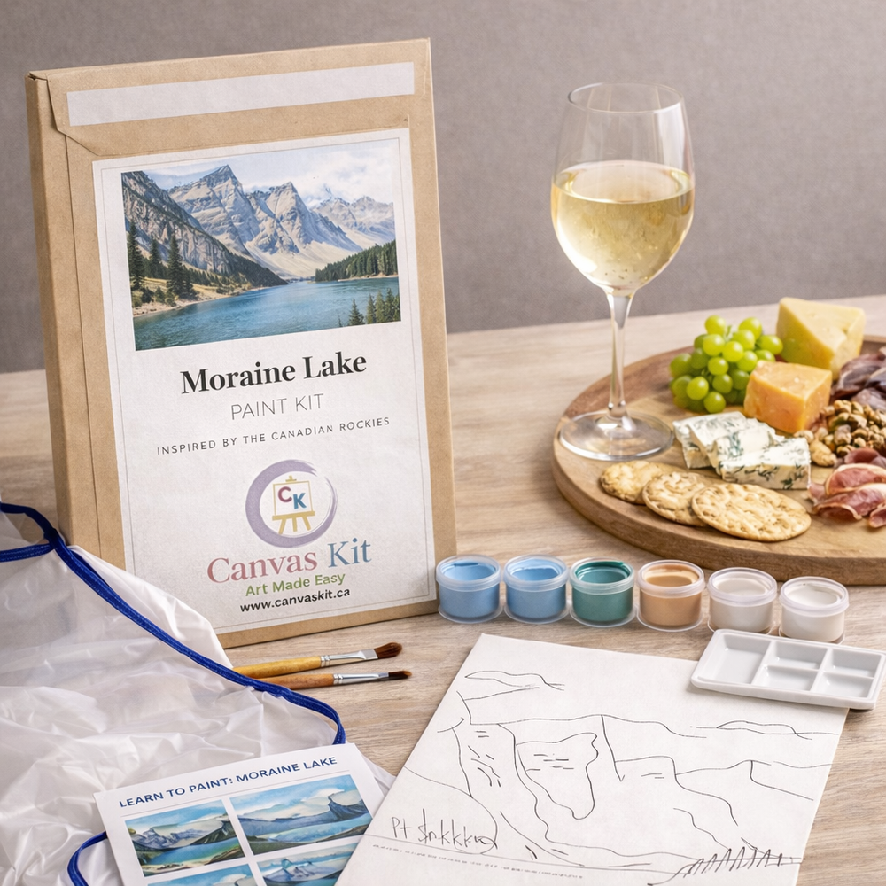 Canvas paint kit with mountain scene, wine glass, and appetizer platter on a wooden table.