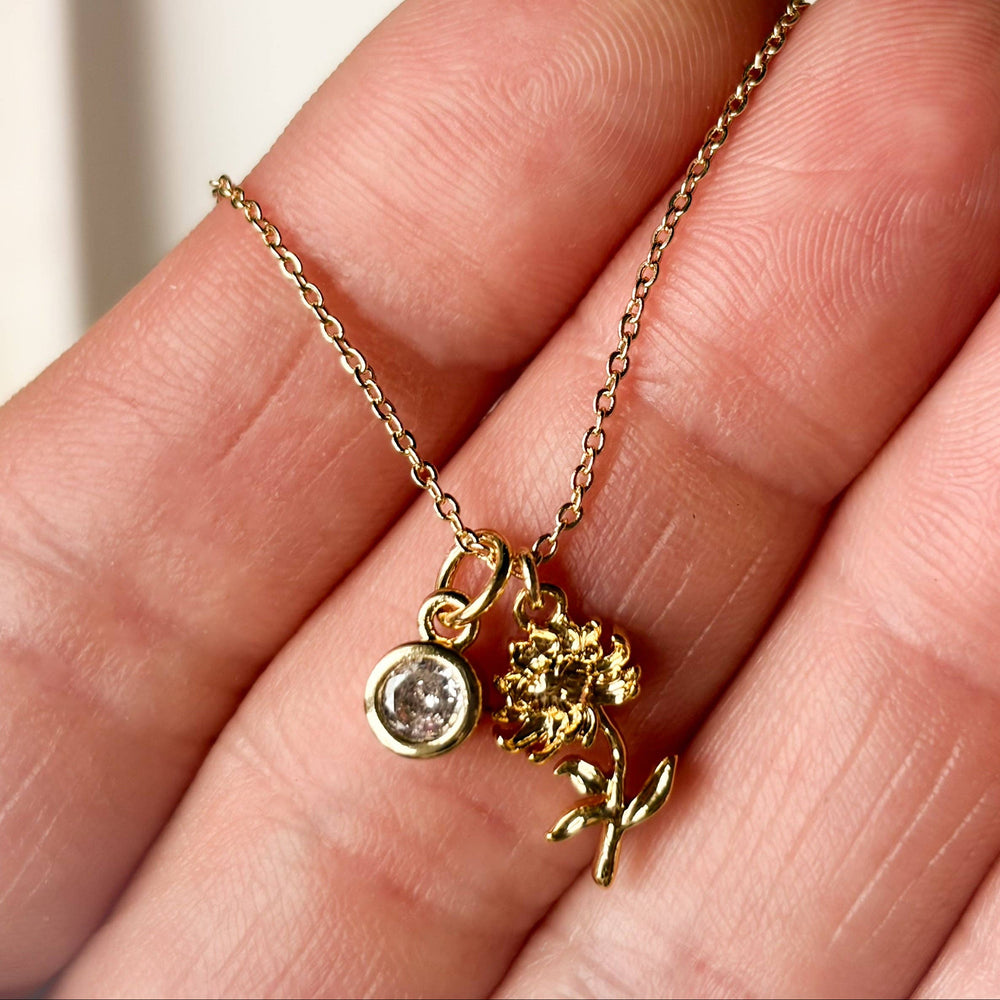 Gold necklace with a flower pendant held in a hand against a neutral background