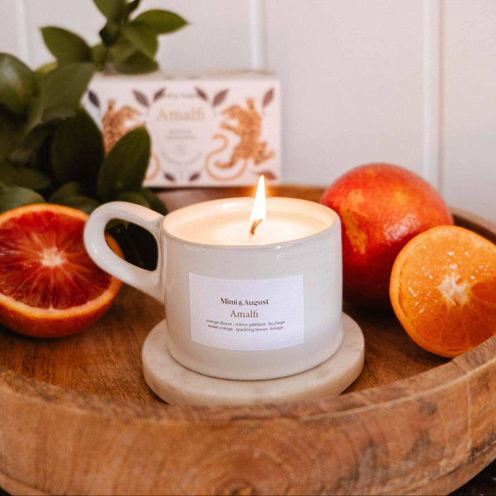 Candle in a mug on a wooden tray with fruits and a soap bar in the background