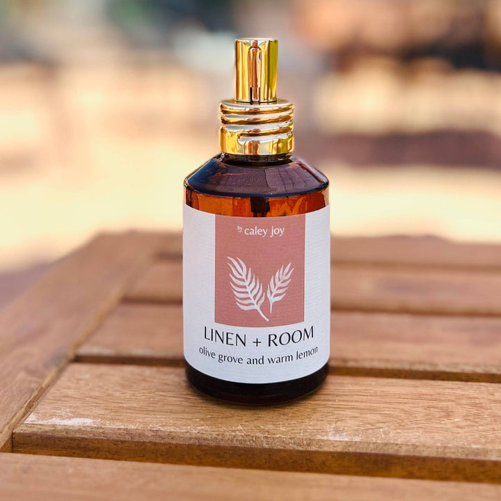 A small amber glass spray bottle with a gold cap and a white label reading &