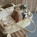 Wicker basket with baby items including a blanket, bottle, and toys on a checkered chair.