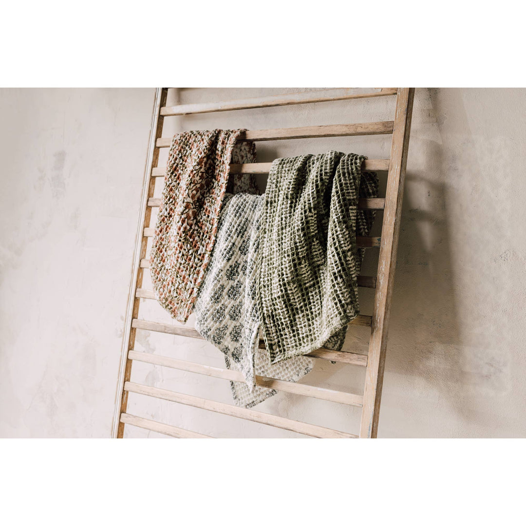 Wooden ladder with patterned towels on a plain background