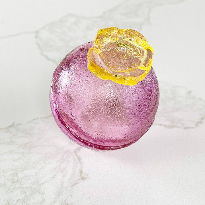 Pink glass object with a yellow top on a marble surface
