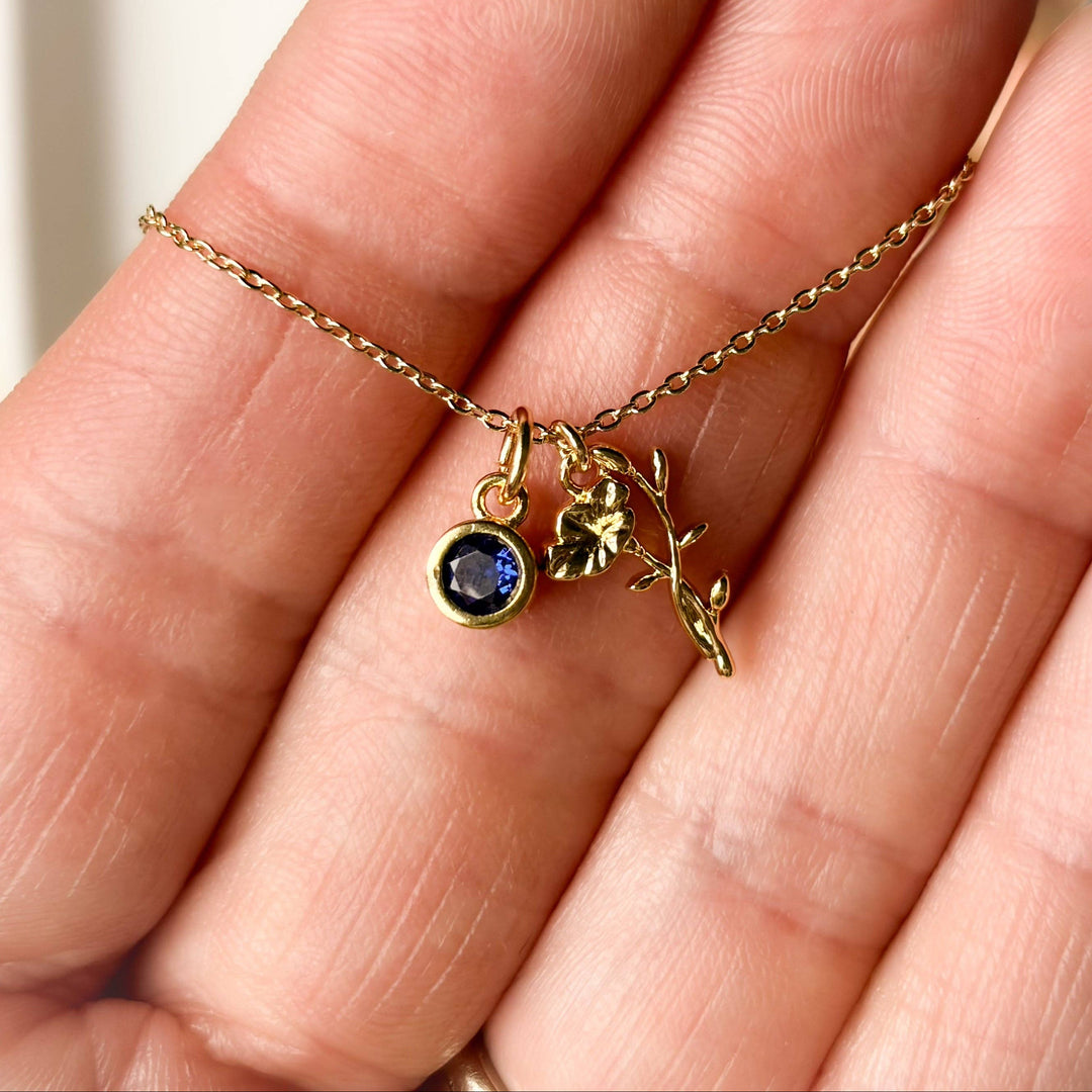 Gold necklace with a blue gemstone pendant held between fingers