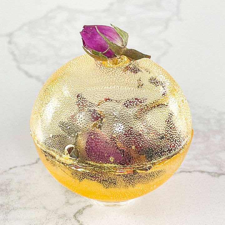 Gold bath bomb with a pink rose on a marble surface