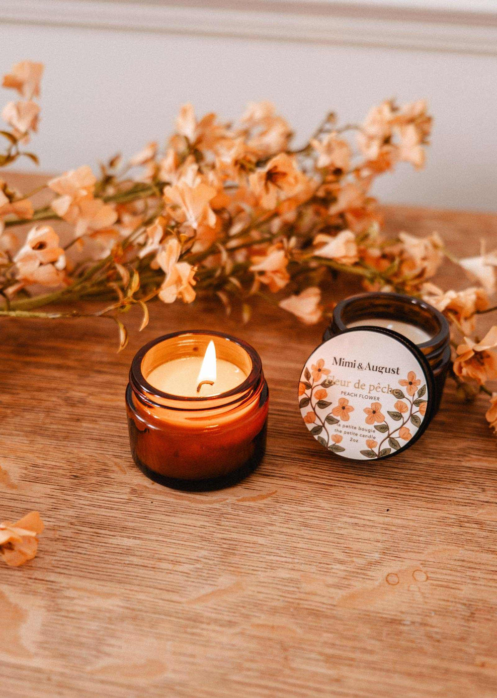 Candle and packaging on a wooden surface with flowers in the background