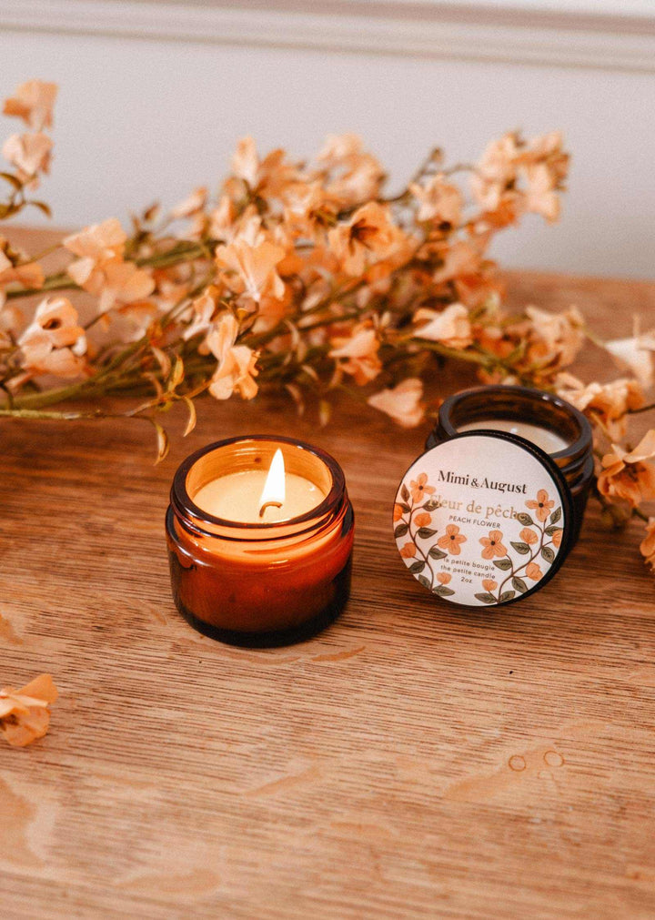 Candle and packaging on a wooden surface with flowers in the background