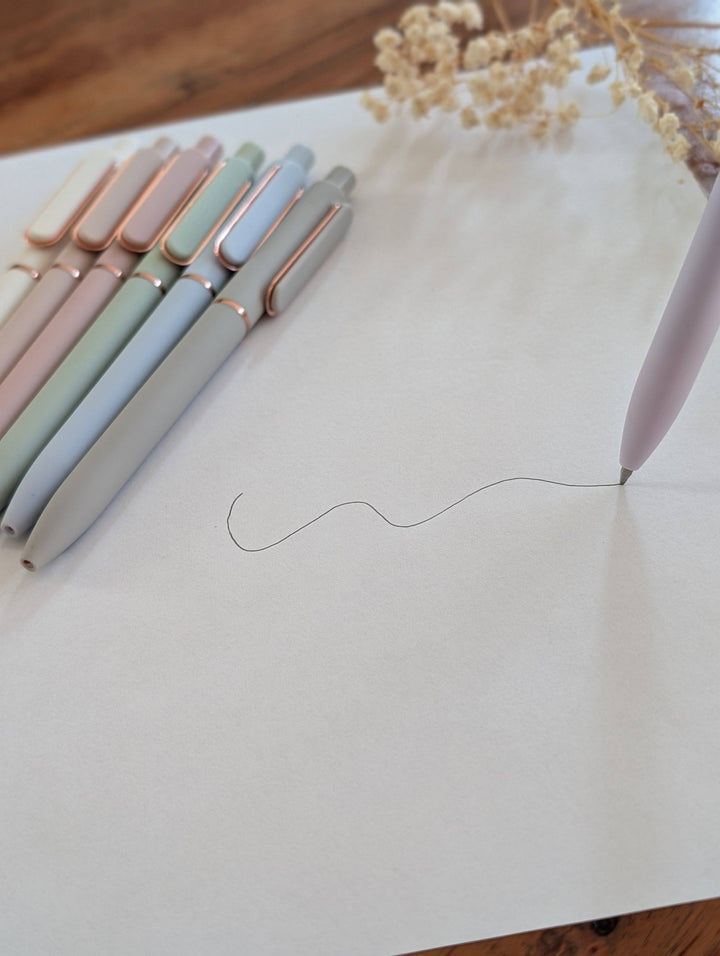 Set of pastel-colored pens on a white surface with a wooden background