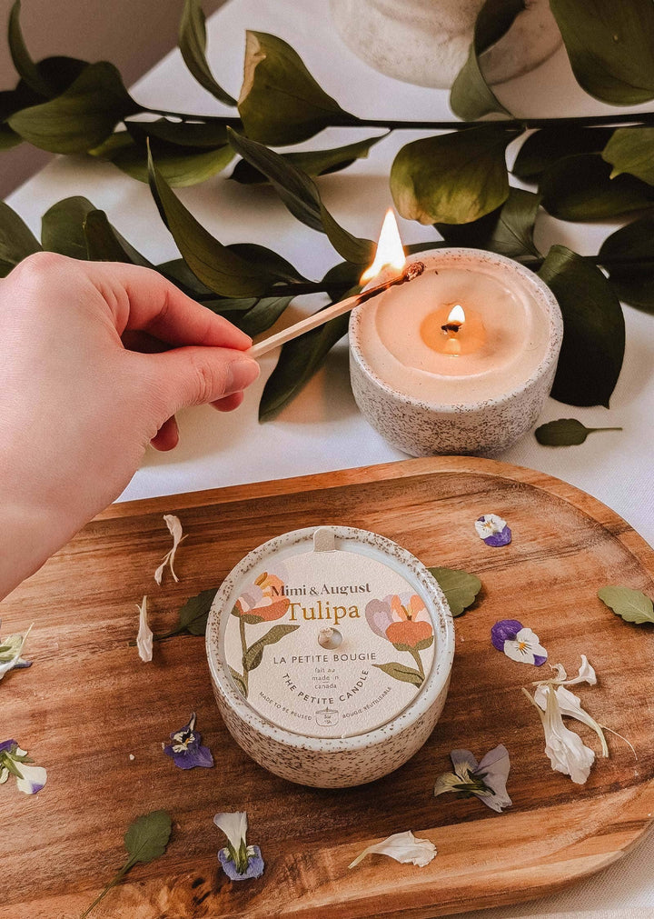 Hand lighting a candle on a wooden board with a container labeled &