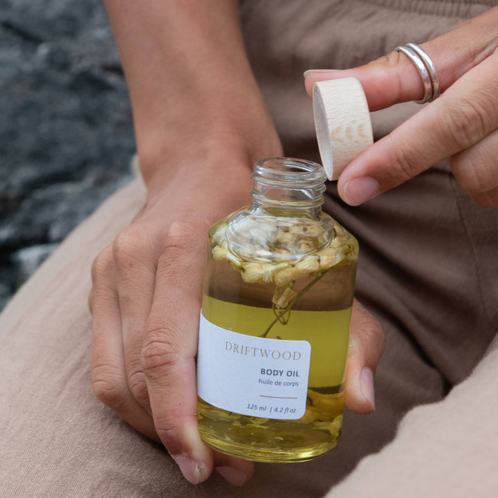 Person holding a bottle of Driftwood Body Oil with a blurred natural background