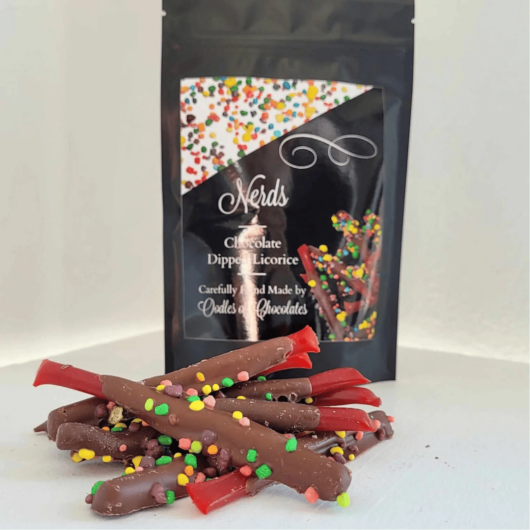 Chocolate-dipped licorice with colorful sprinkles next to a black packaging bag featuring colorful sprinkles.