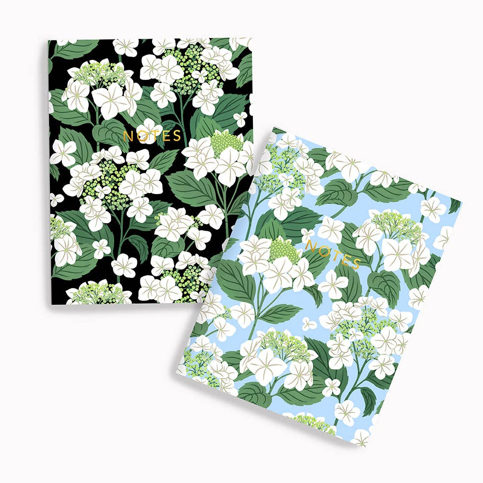 Two floral notebooks with black and white flowers on one and green and white flowers on the other, on a white background.
