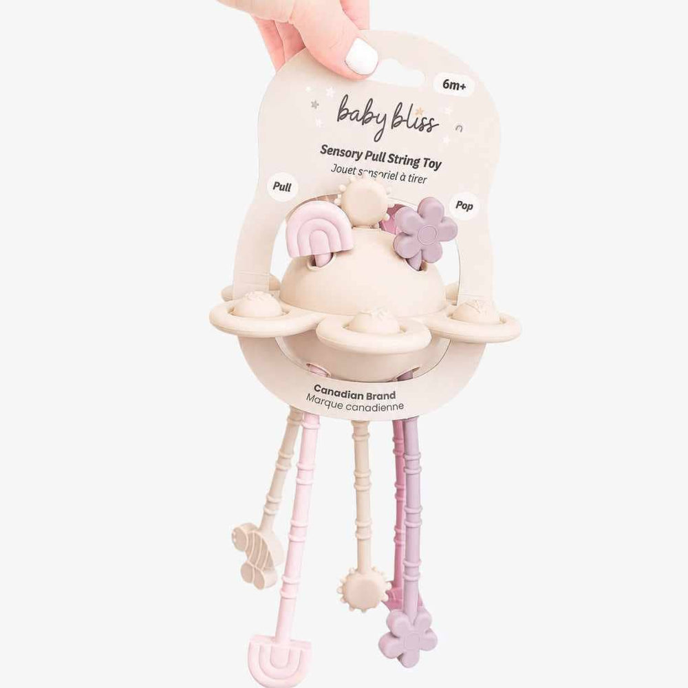 Baby bliss Sensory Pull String Toy in a pastel cream, pink, and lavender color scheme, held by a hand against a light gray background.