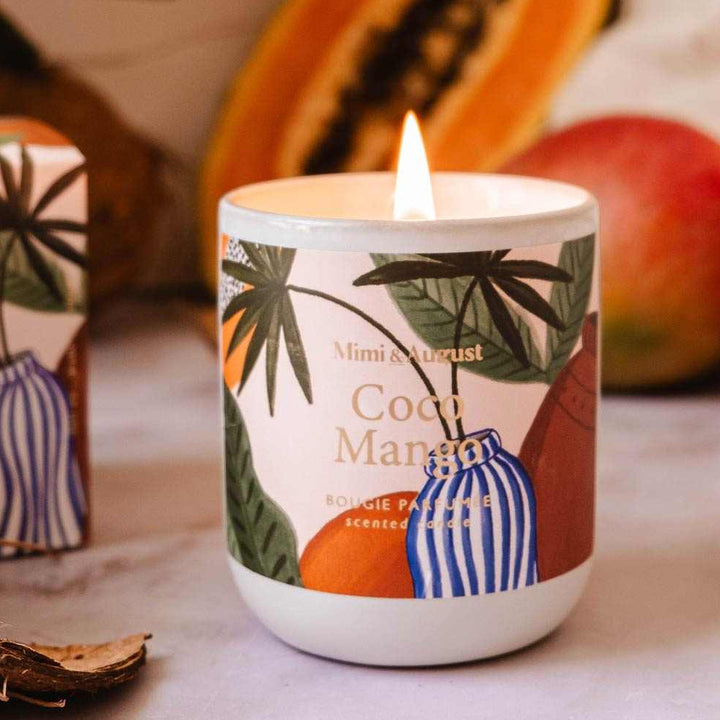 Candle with tropical design surrounded by fruits and leaves on a textured surface