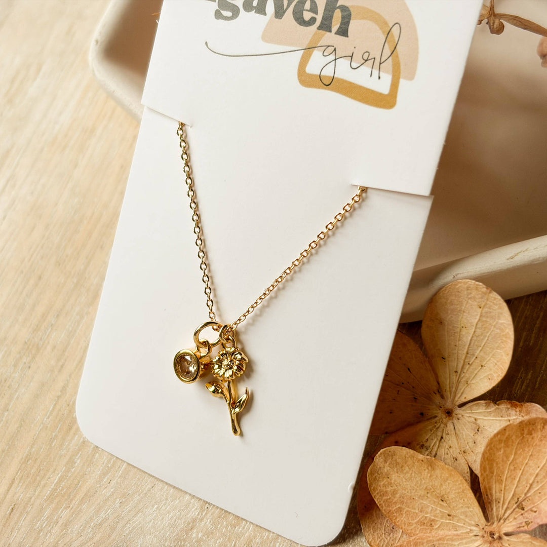Gold necklace on a 'Gavea Girl' branded card with dried flowers in the background