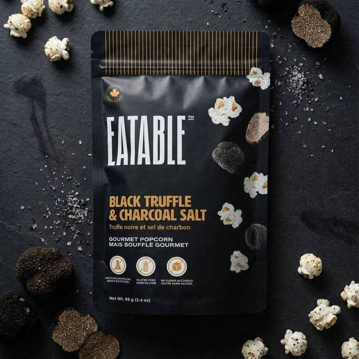 Eatable Black Truffle &amp; Charcoal Salt popcorn package on a dark surface with truffles and popcorn.