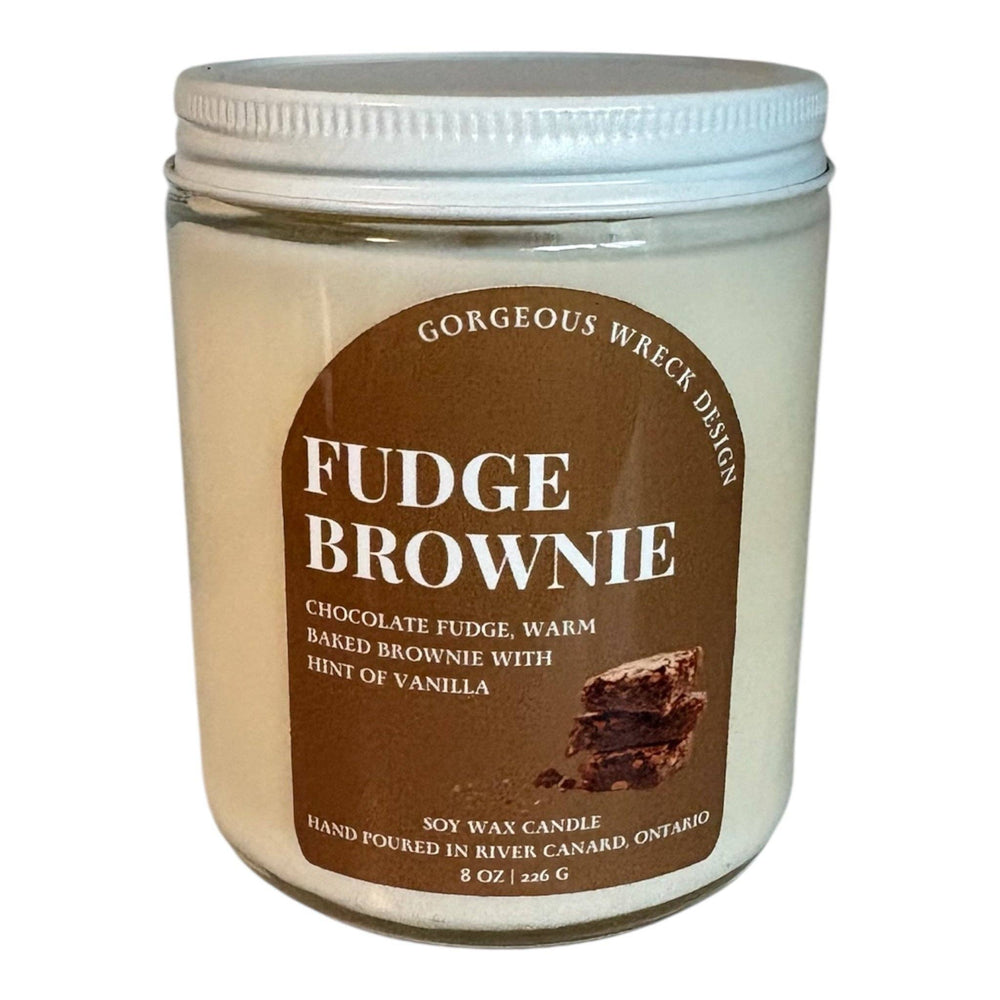 An 8 oz soy wax candle in a clear glass jar with a white screw-top lid, featuring a brown label that reads 'FUDGE BROWNIE' and shows a brownie slice graphic.