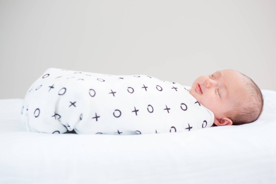Newborn baby swaddled in a white blanket with black patterns on a light gray background