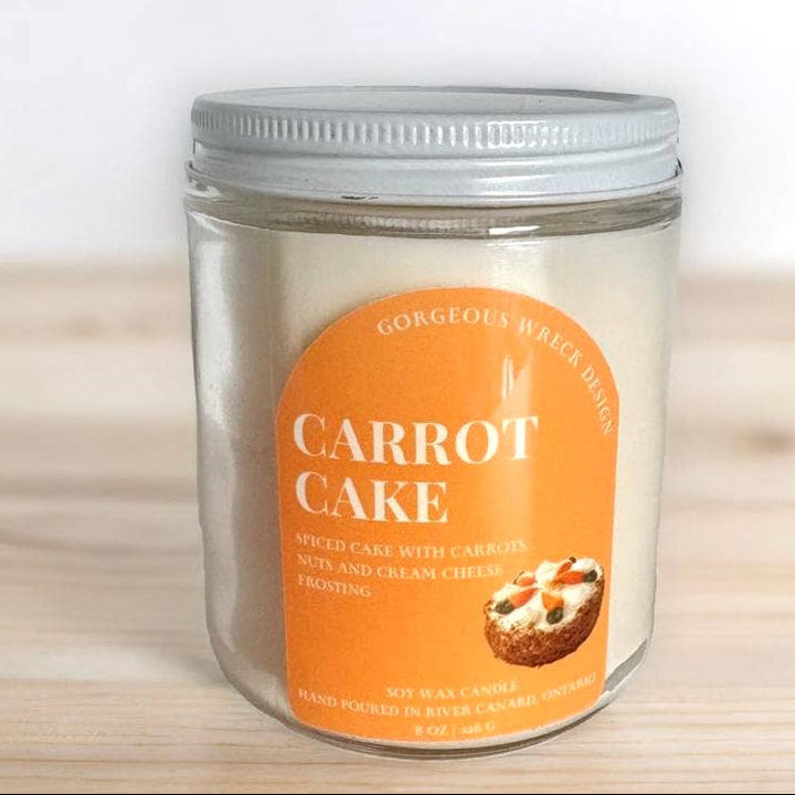 A glass jar candle with a silver metal lid and a prominent orange label reading &