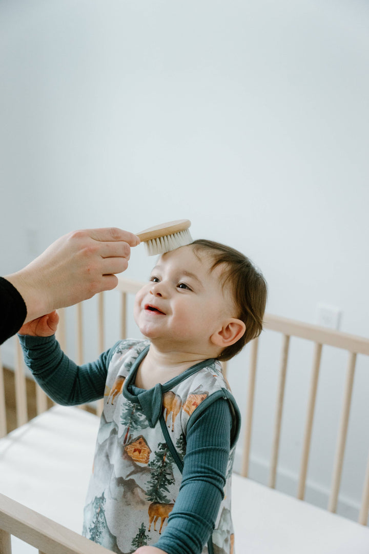 Child being brushed by an adult in a crib with a white background