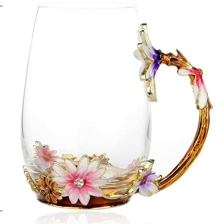 A clear glass mug with a gold-toned floral handle and pink, white, and purple enamel flowers at the base, shown alongside a red soda can for scale. The image includes dimension labels: 5.