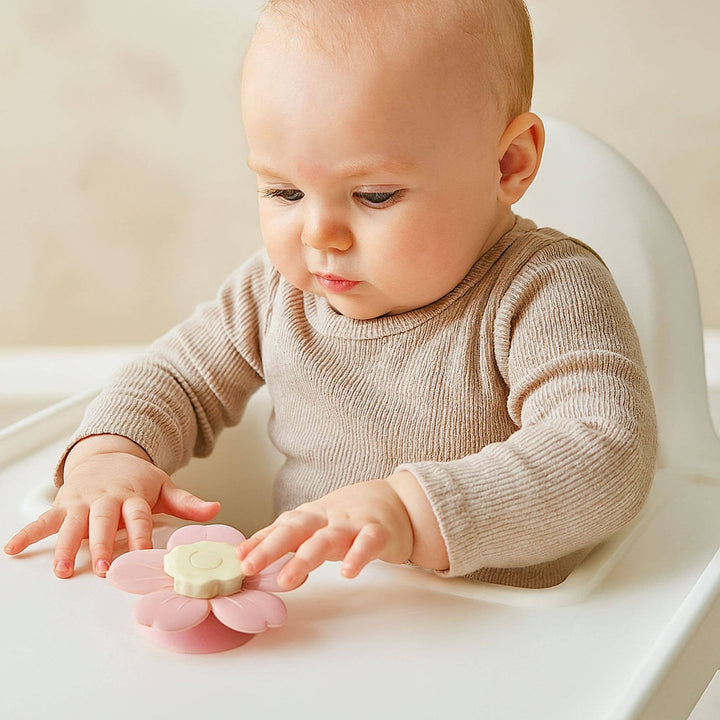 Baby in a high chair playing with a pink toy