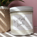Candle jar labeled 'West Coast Woods' on a surface with a plant in the background