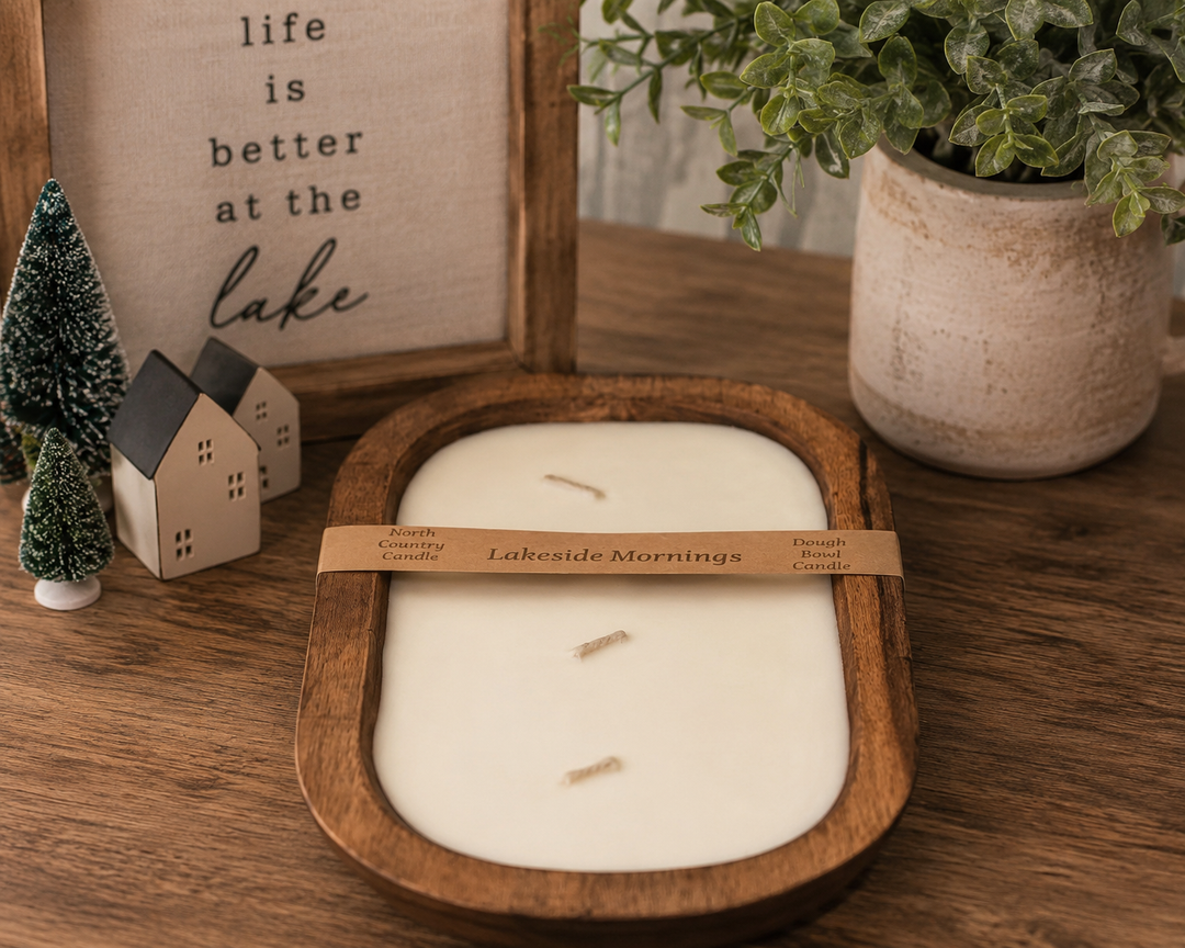 A wooden tray candle with cream-colored wax and three wicks, wrapped in a tan paper band reading &