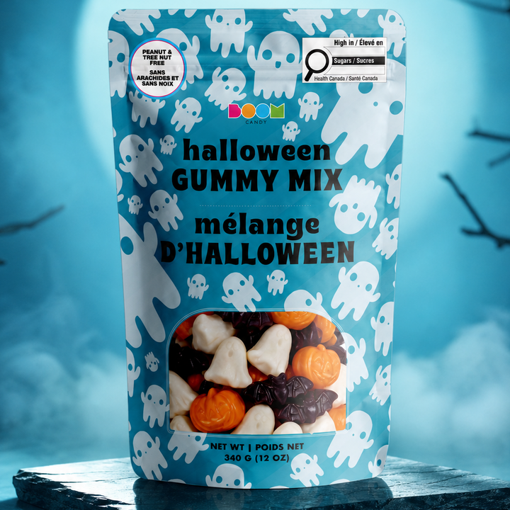 A stand-up pouch of Halloween gummy mix with a blue background and white ghost illustrations, displayed on a dark stone slab against a spooky blue backdrop with mist and bare tree branches.