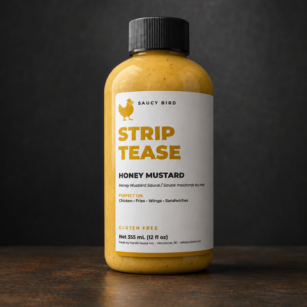 A bottle of Saucy Bird Strip Tease Honey Mustard sauce, 340 mL, standing on a dark wooden surface against a dark gray background.