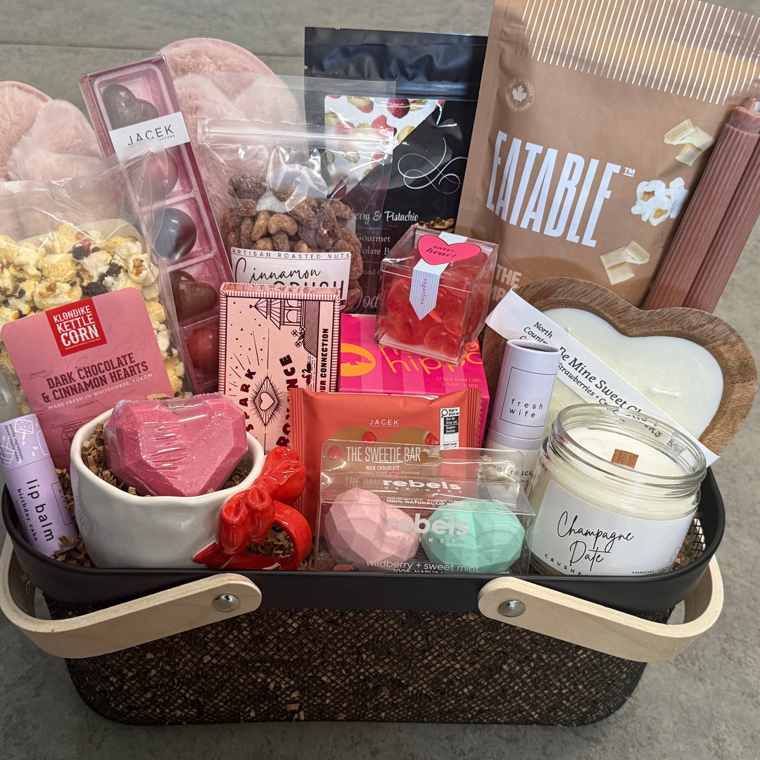 Gift basket with various items including a candle, snacks, and bath bombs on a concrete surface.