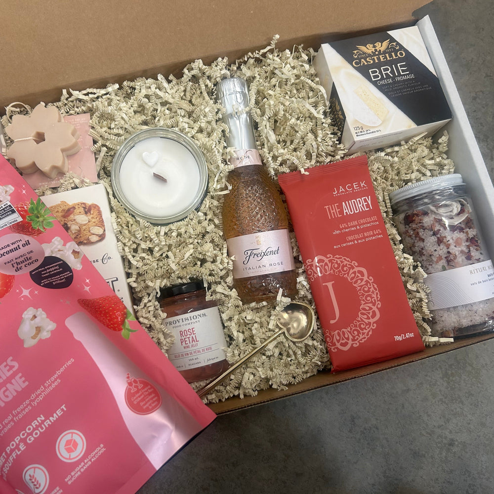 Gift box with champagne, snacks, and a candle on a concrete surface