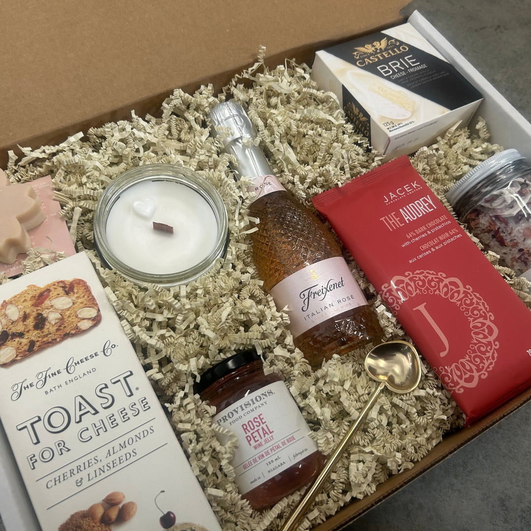 Gift box with assorted items including a bottle, candles, and packaging on a neutral background