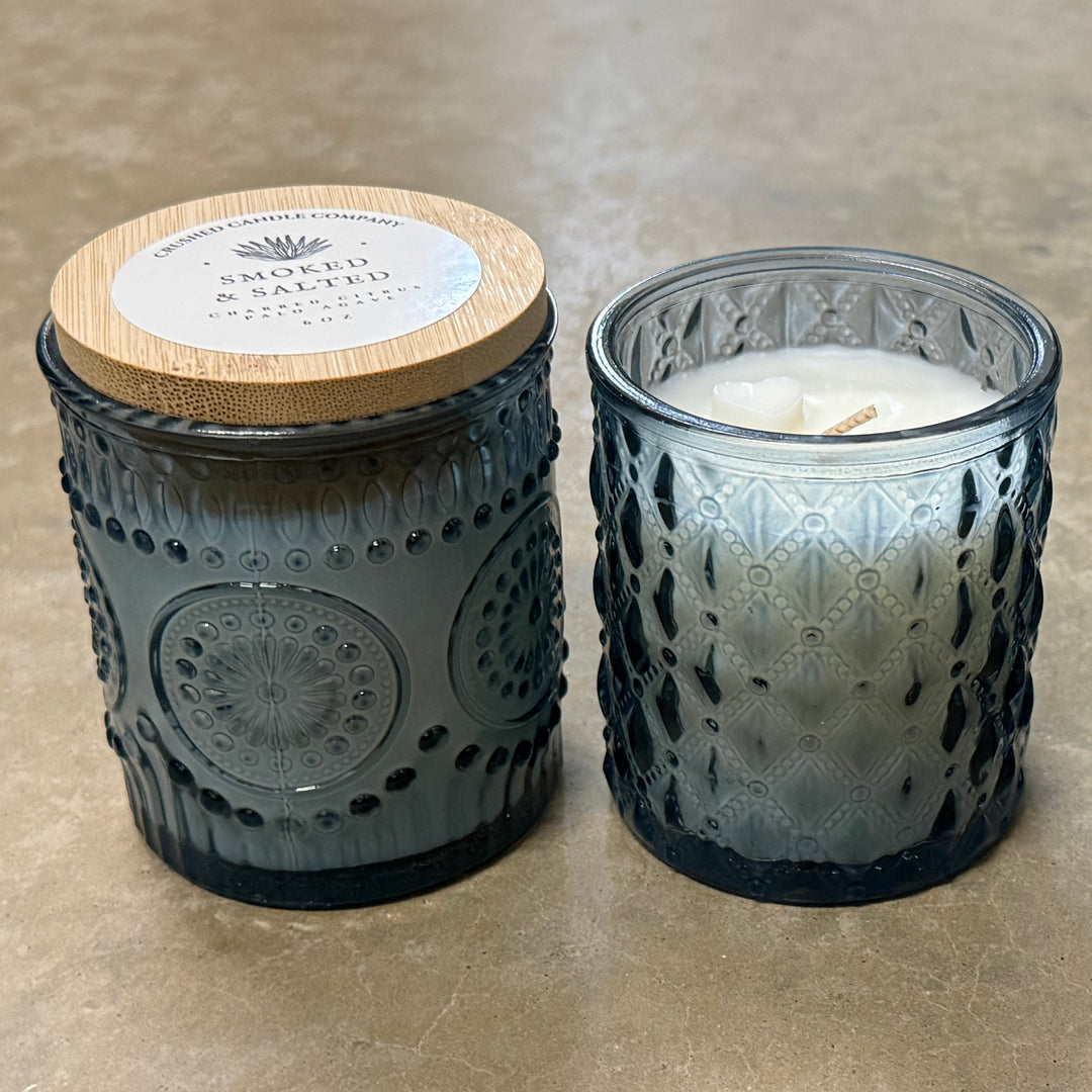 Three textured glass candles with wooden lids on a concrete surface