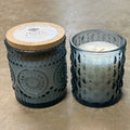 Three textured glass candles with wooden lids on a concrete surface