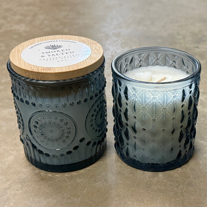 Three textured glass candles with wooden lids on a concrete surface