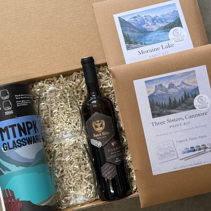 Box containing a bottle of wine, glassware, and paint kit with mountain-themed labels.