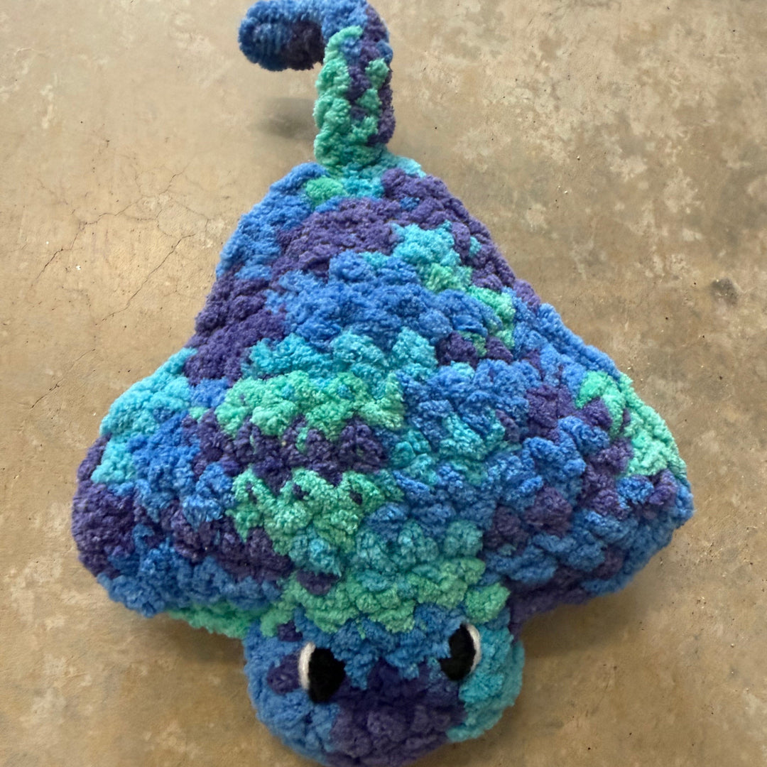 Crocheted blue and green fish toy on a beige surface