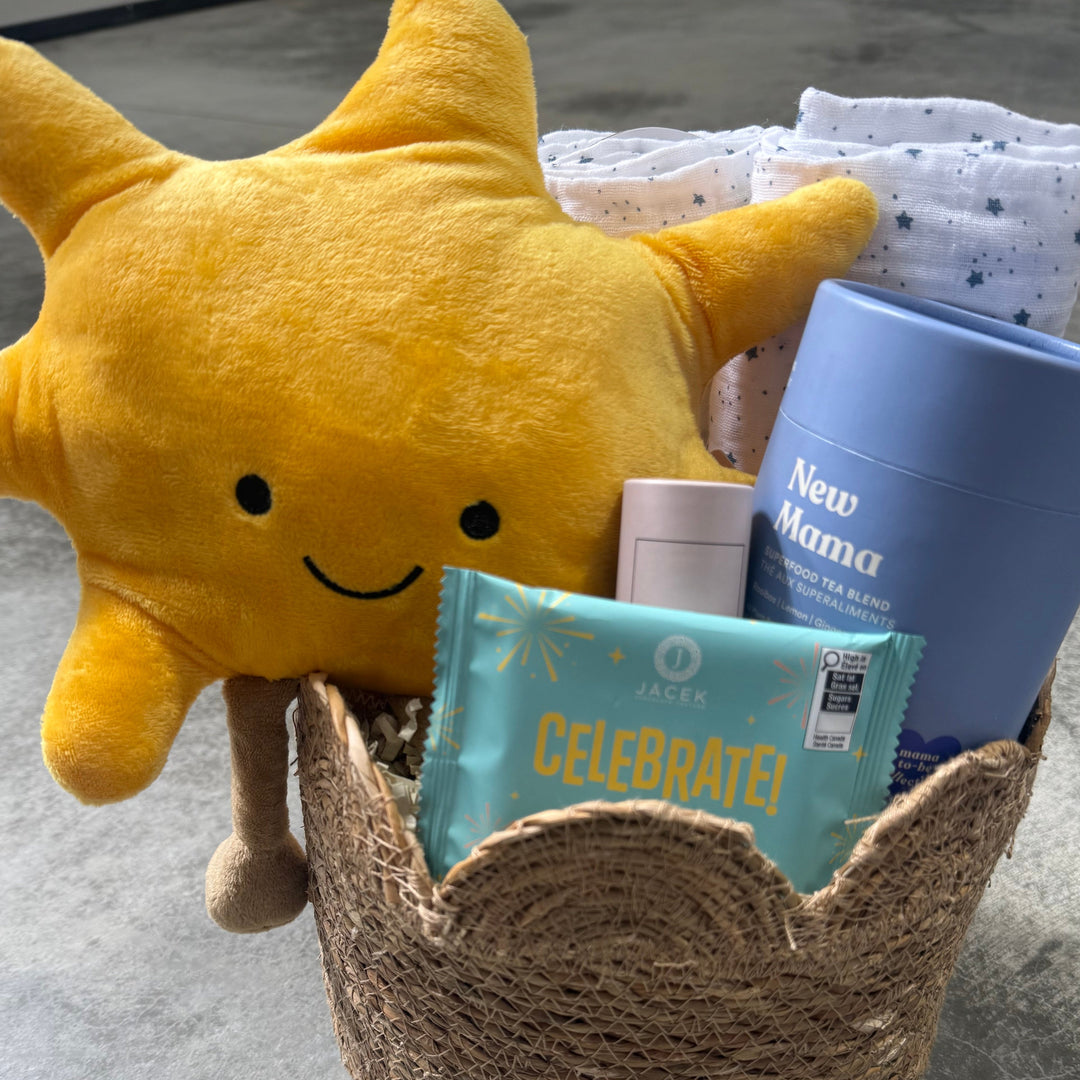 Yellow plush sun toy with baby items including a blue book and cards in a woven basket on a concrete floor.
