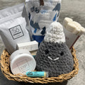 Basket with various items including a crocheted mountain, soap, and other products on a concrete surface.
