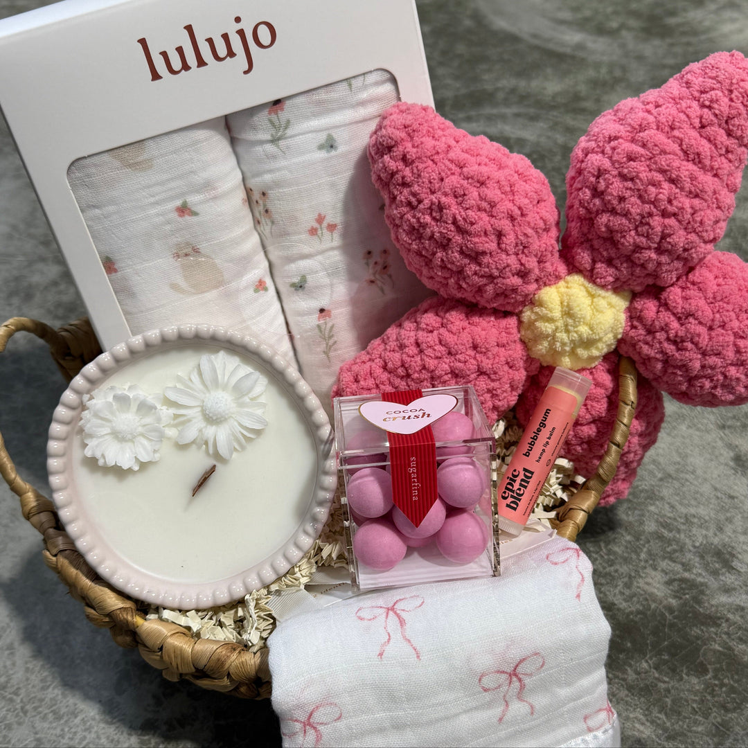 Lulujo baby products including a basket, candle, and flowers on a textured surface