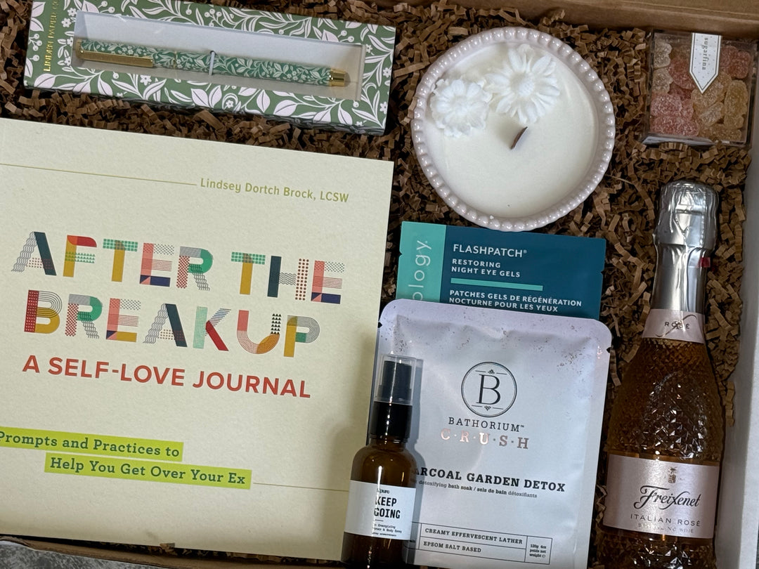 A curated self-care and relationship gift box arranged in brown packing material, featuring a journal titled &