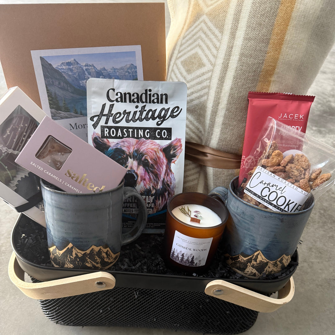 Gourmet gift basket with mugs, snacks, and a candle on a tray.