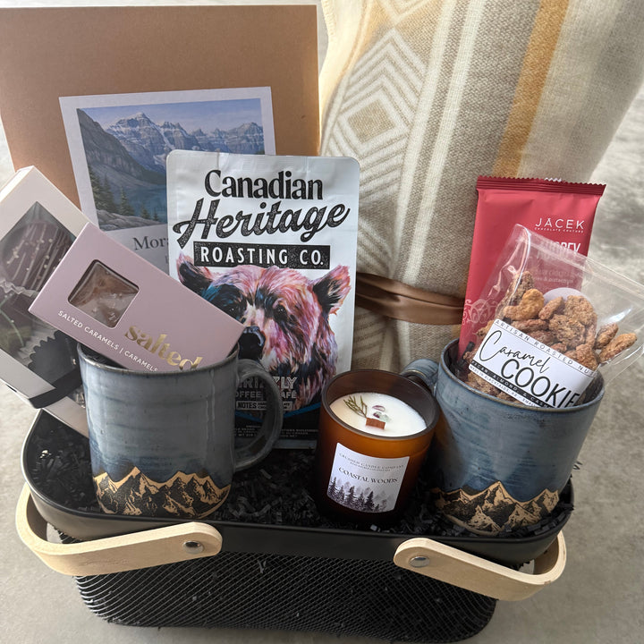 Gourmet gift basket with mugs, snacks, and a candle on a tray.