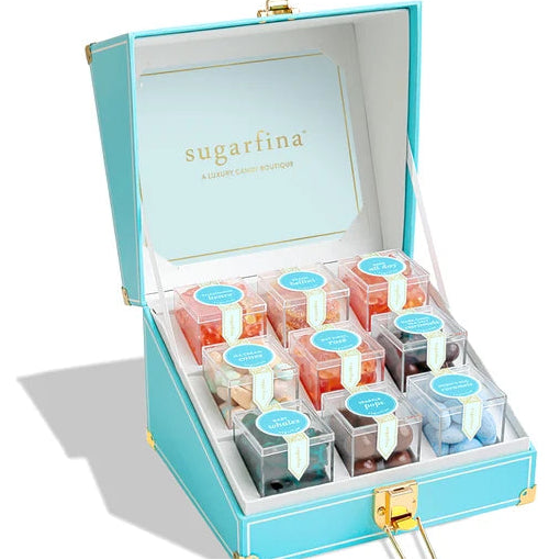 An open turquoise Sugarfina enamel candy box with gold-tone hardware, displaying multiple small clear plastic candy containers arranged in a white interior. The brand name &